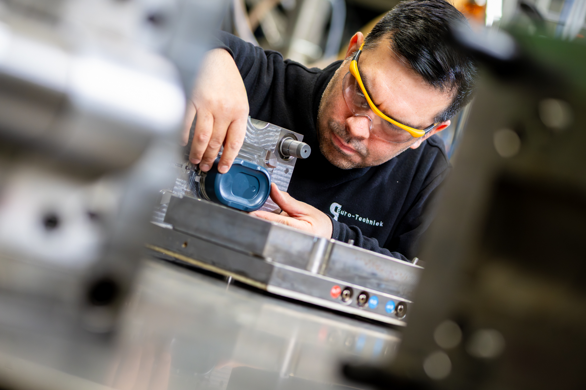 Man monteert metaalonderdeel, draagt veiligheidsbril.